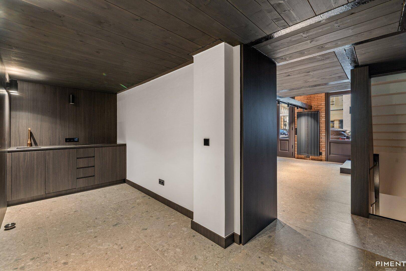 Moderner Küchenbereich mit dunklen Holzschränken, Steinboden und weißer Wand.
