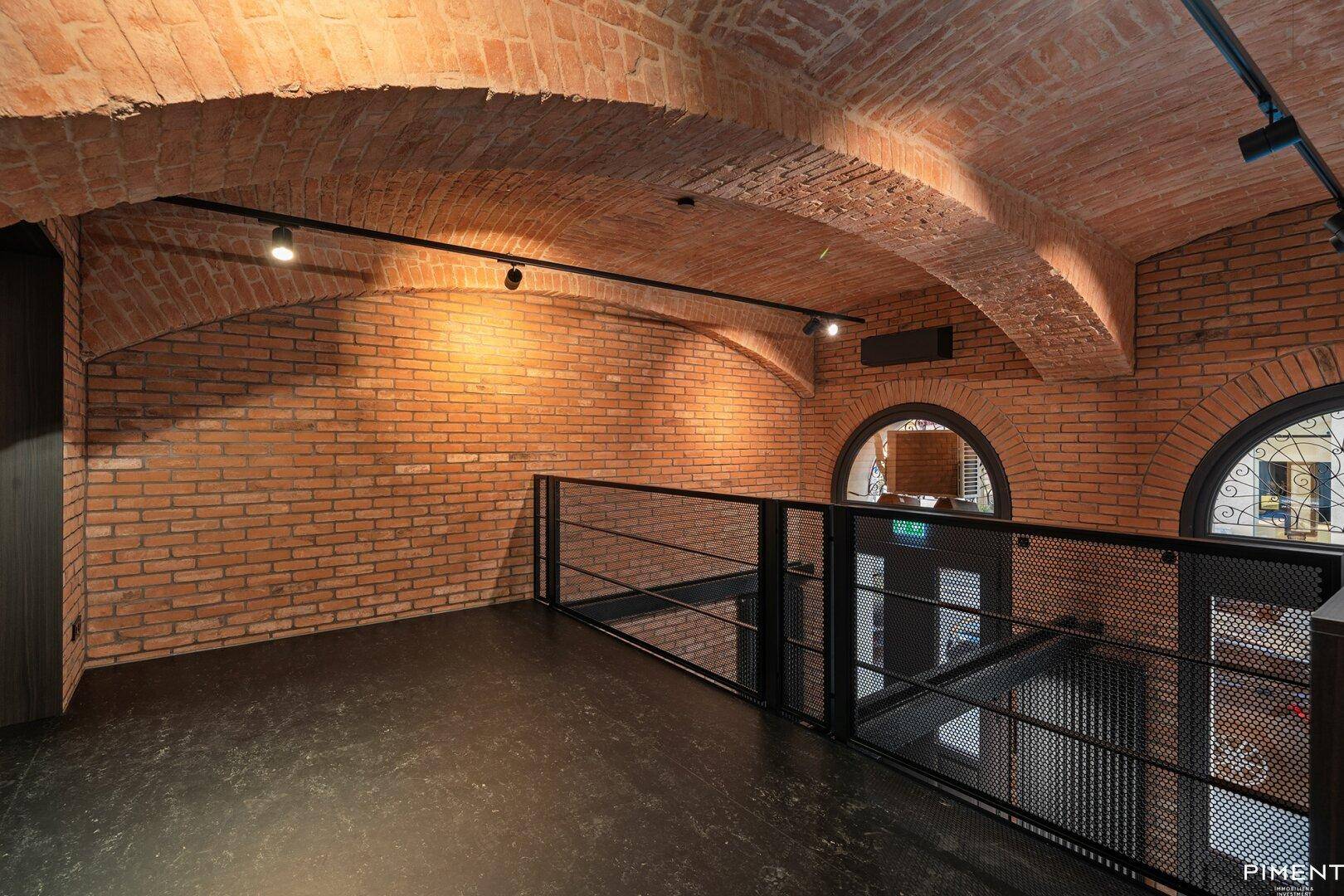 Obere Galerie mit Ziegelgewölbedecke, schwarzem Boden und Metallgeländer.