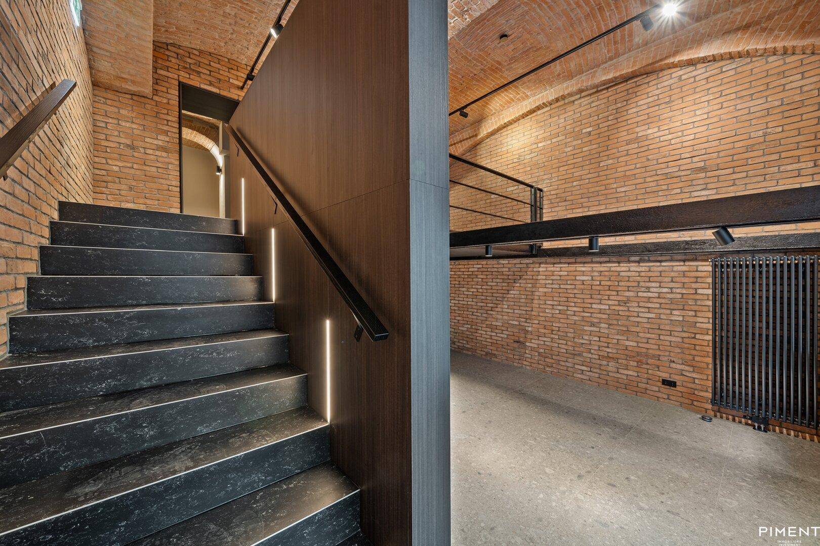 Moderne Treppe mit dunklen Stufen, integrierter Beleuchtung und Ziegelwänden.