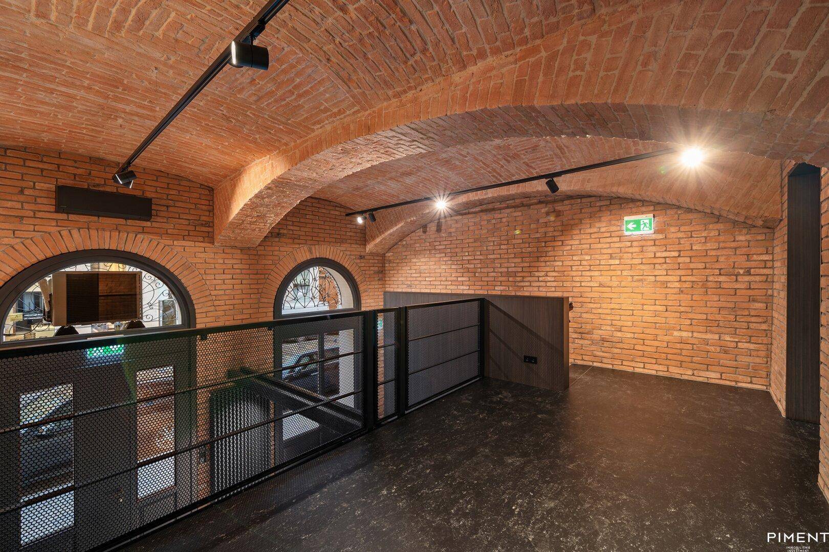 Geräumige Galerie mit freiliegenden Ziegeln, Gewölbedecke und Blick auf den unteren Bereich.