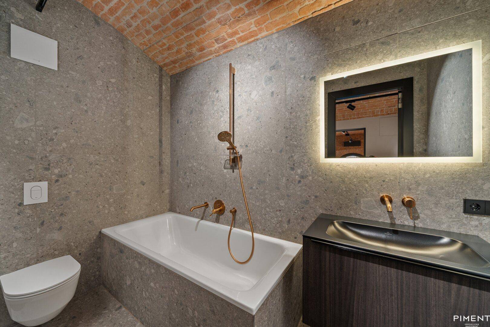 Elegantes Badezimmer mit Badewanne, Steinwänden und modernen Armaturen in Kupferoptik.