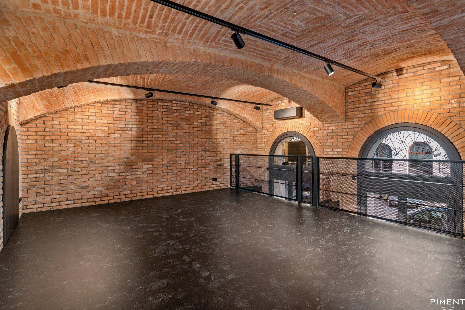 Obere Galerieebene mit freiliegenden Ziegelwänden, beeindruckender Gewölbedecke und Rundbogenfenstern.