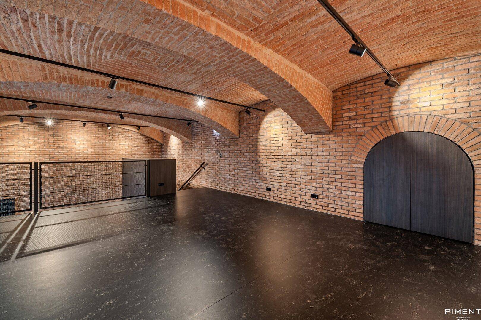 Lange Galerieebene mit freiliegenden Ziegelwänden, Gewölbedecke und einem eleganten Rundbogeneingang.