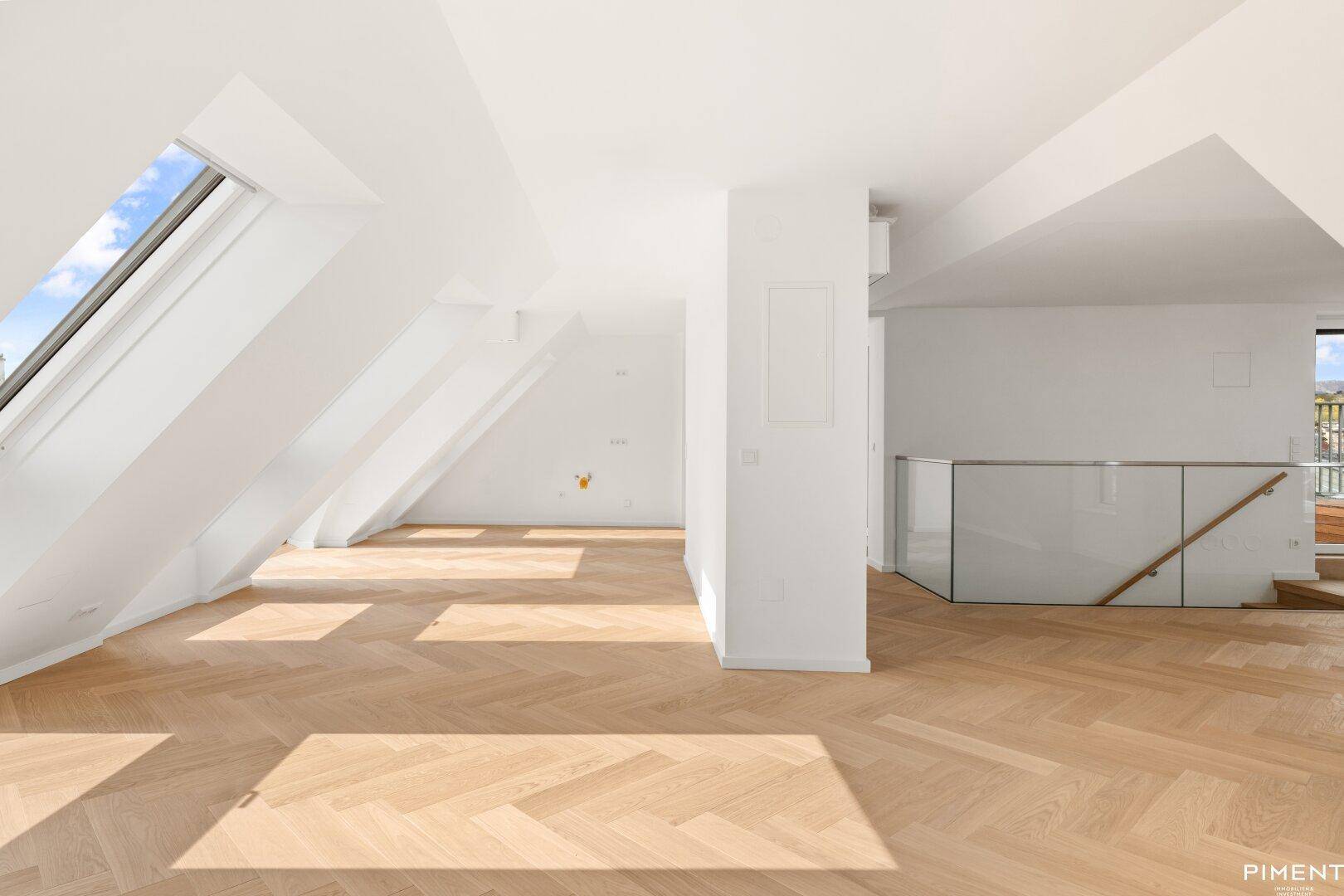 Geräumiges Dachgeschosszimmer mit viel Tageslicht, schrägen Wänden und moderner Treppe.