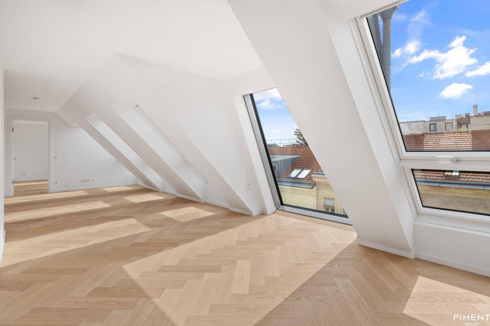 Lichtdurchfluteter Dachgeschossraum mit großen Dachfenstern und Blick auf die Stadt.