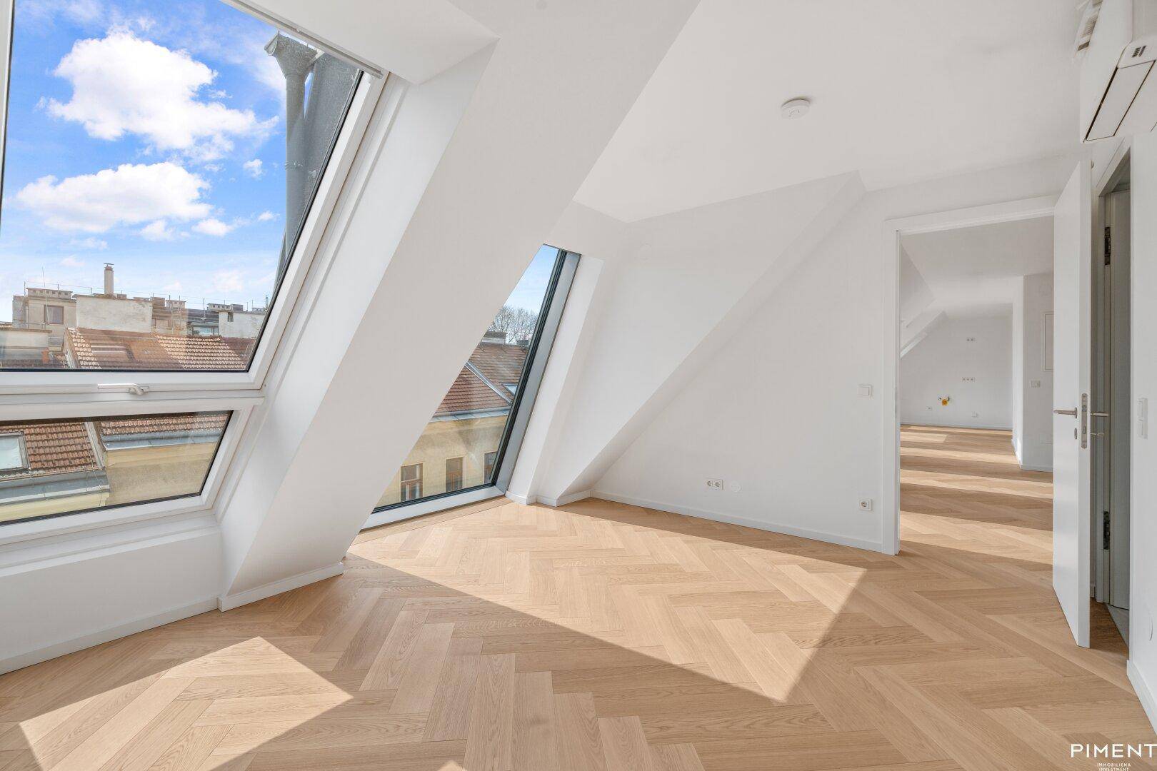 Geräumiges Dachgeschosszimmer mit schrägen Wänden, großen Fenstern und hellem Parkettboden.