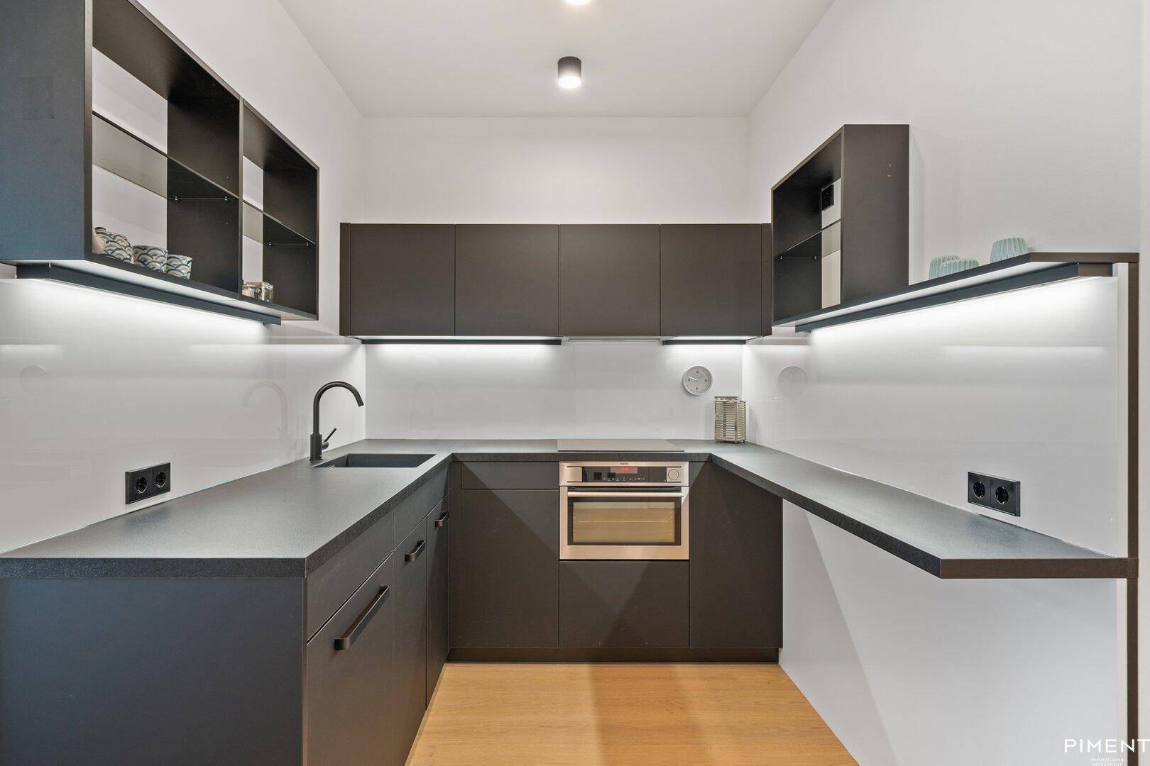 Moderne Einbauküche mit dunklen Schränken, integrierten Geräten und heller Arbeitsplattenbeleuchtung.