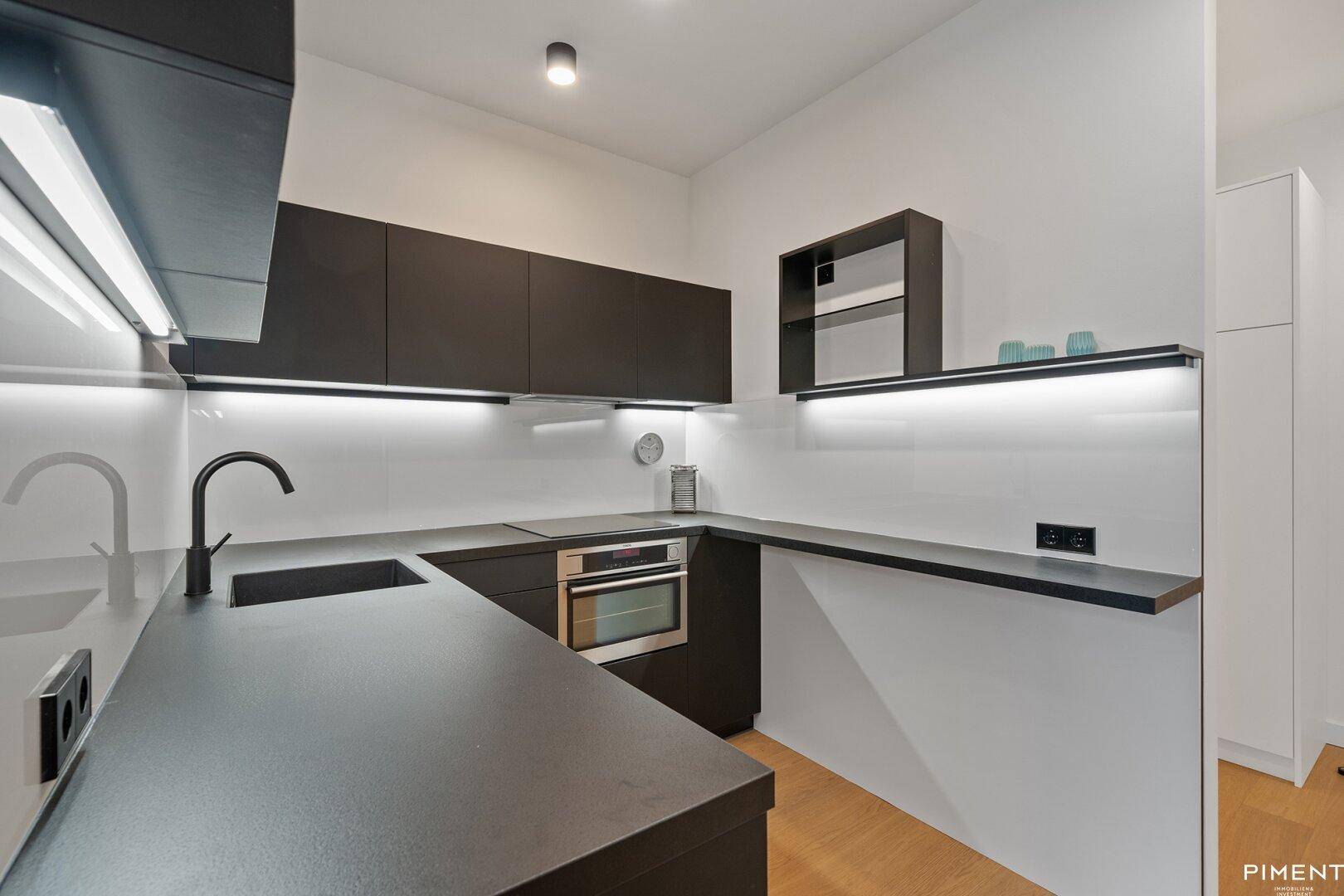 Stilvolle Küche mit dunklen Unterschränken, integriertem Backofen und minimalistischem Design.