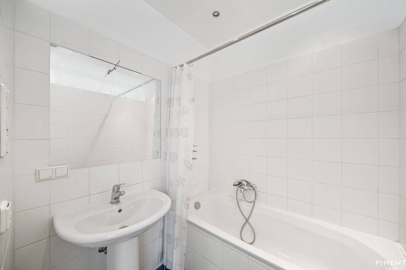 Einfaches Badezimmer mit Badewanne, Waschbecken und weißen Fliesen.