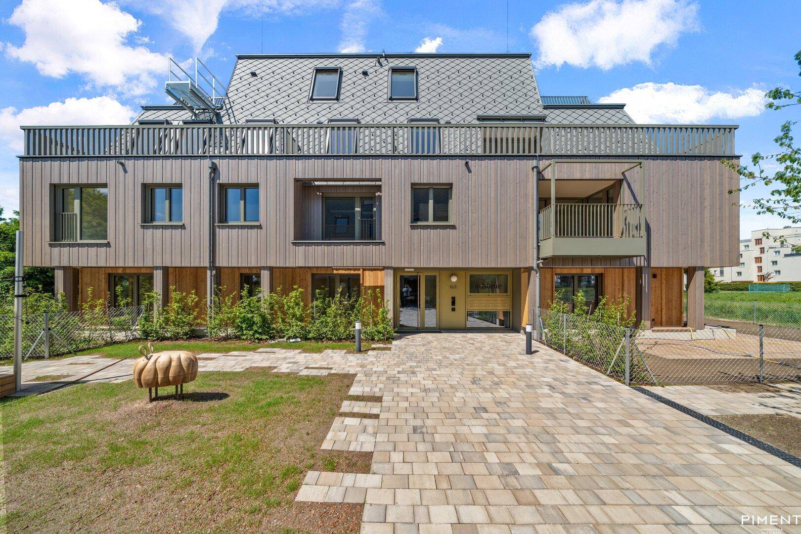 Ansicht der modernen Wohnanlage mit Holzfassade, Balkonen und einem gepflegten Eingangsbereich.