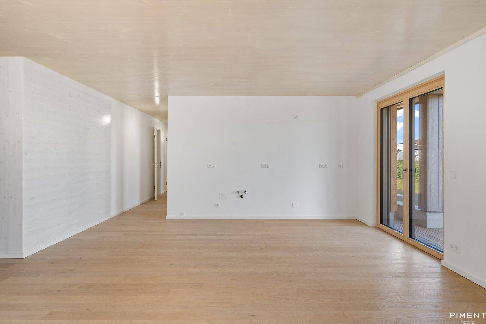 Unmöblierter Wohnbereich mit hellem Holzboden und Holzdecke, bereit für die Installation einer Küche oder Medienwand.