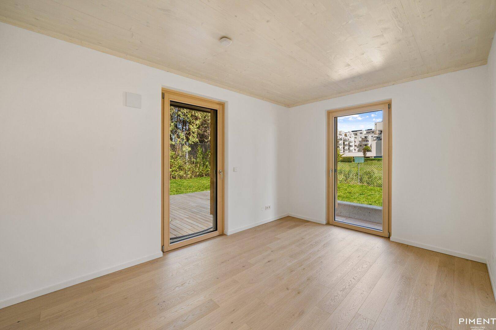 Helles Schlafzimmer mit Holzboden und zwei Glastüren, die direkten Zugang zum Gartenbereich ermöglichen.