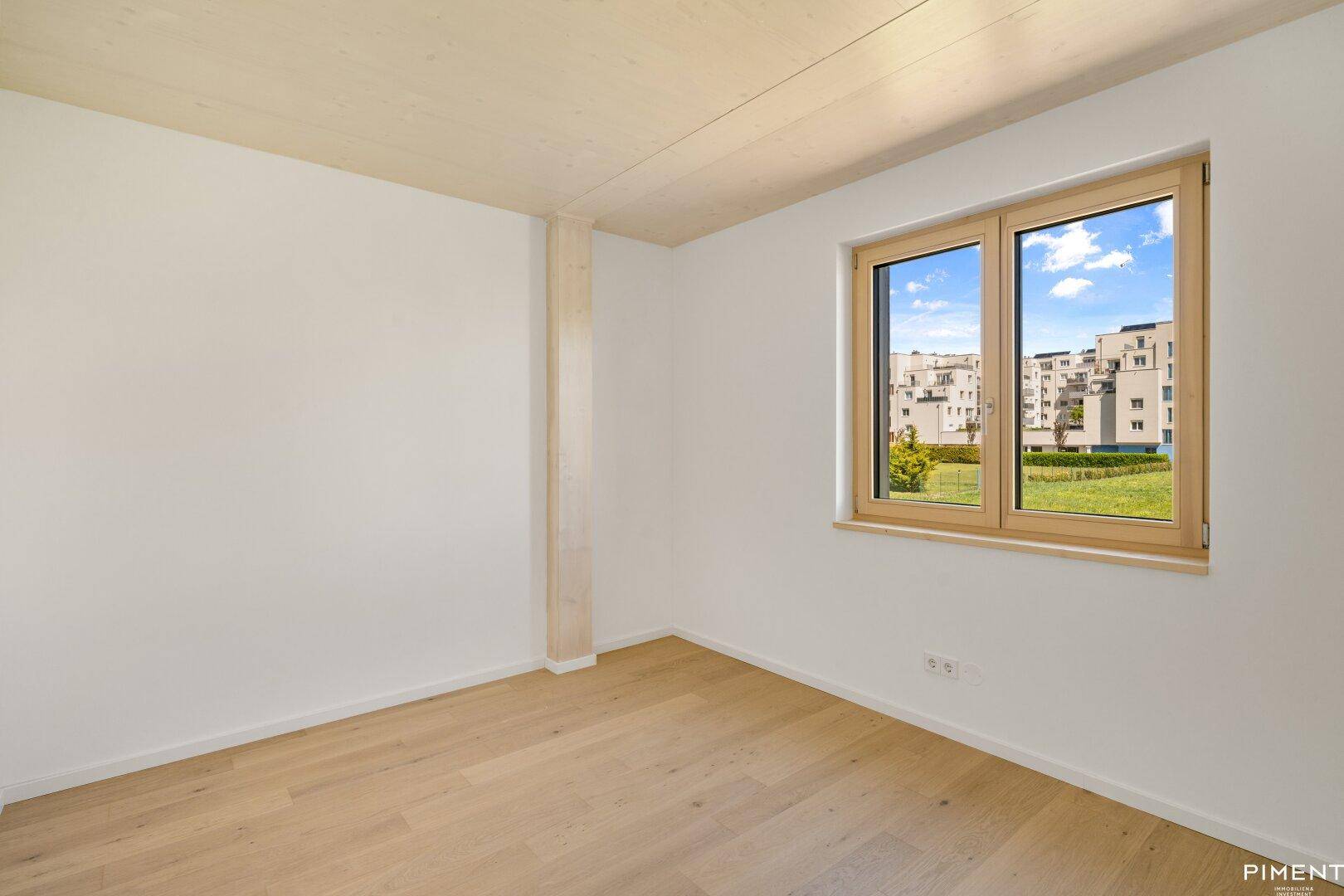 Lichtdurchflutetes Zimmer mit Holzboden und Fenster, das einen weiten Blick bietet.