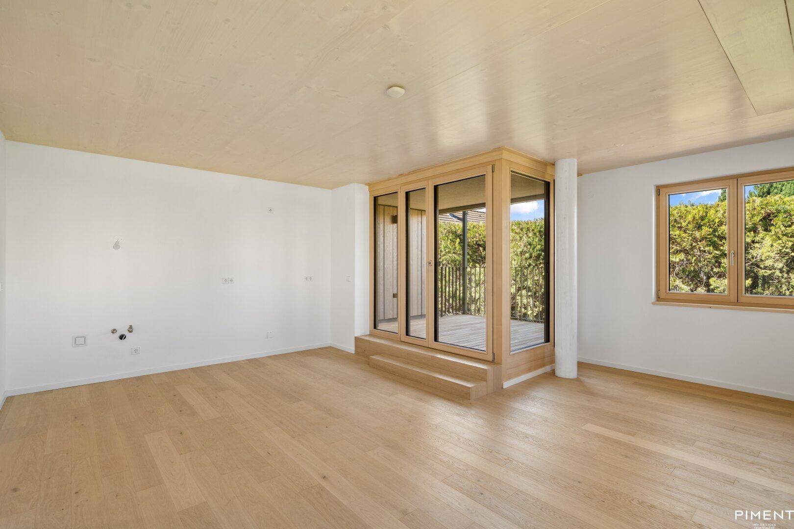 Geräumiges Zimmer mit Holzboden und großen Fenstern, die viel Tageslicht hereinlassen.