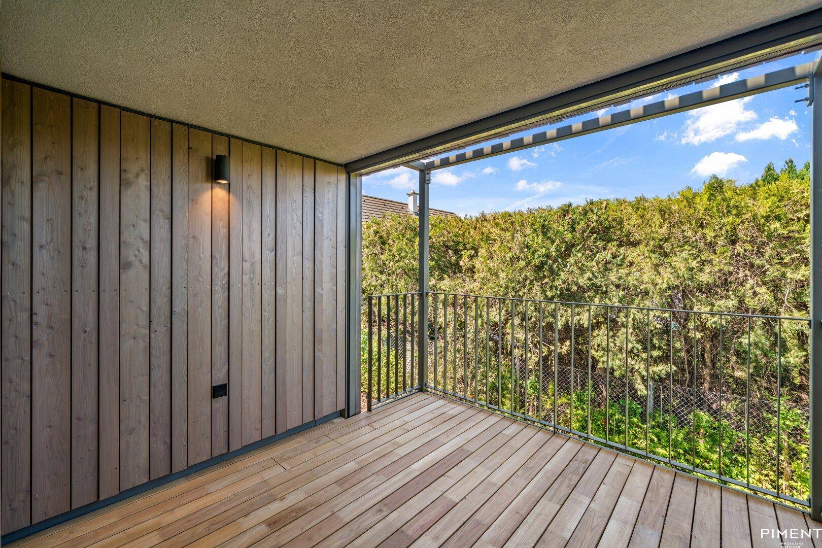 Überdachter Balkon mit Holzwänden und Holzboden, umgeben von üppigem Grün.