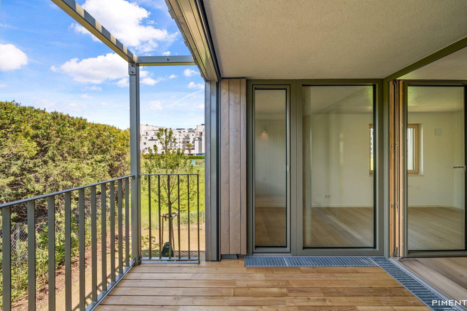 Geräumiger Balkon mit Holzboden und Metallgeländer, bietet Blick auf die grüne Umgebung.