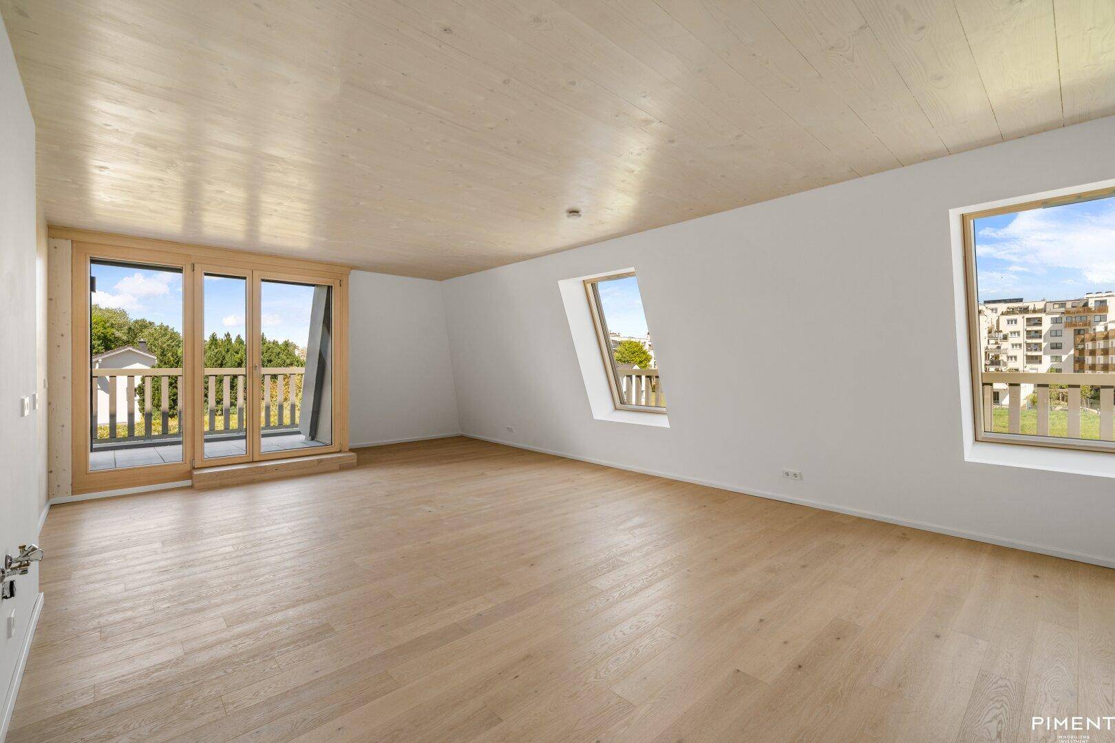 Helles Zimmer mit Holzboden, Dachschrägen und Zugang zu einem Balkon.