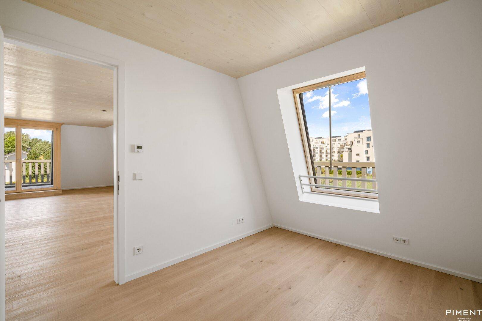 Helles Zimmer mit Holzboden, Dachfenster und Blick auf die Umgebung.