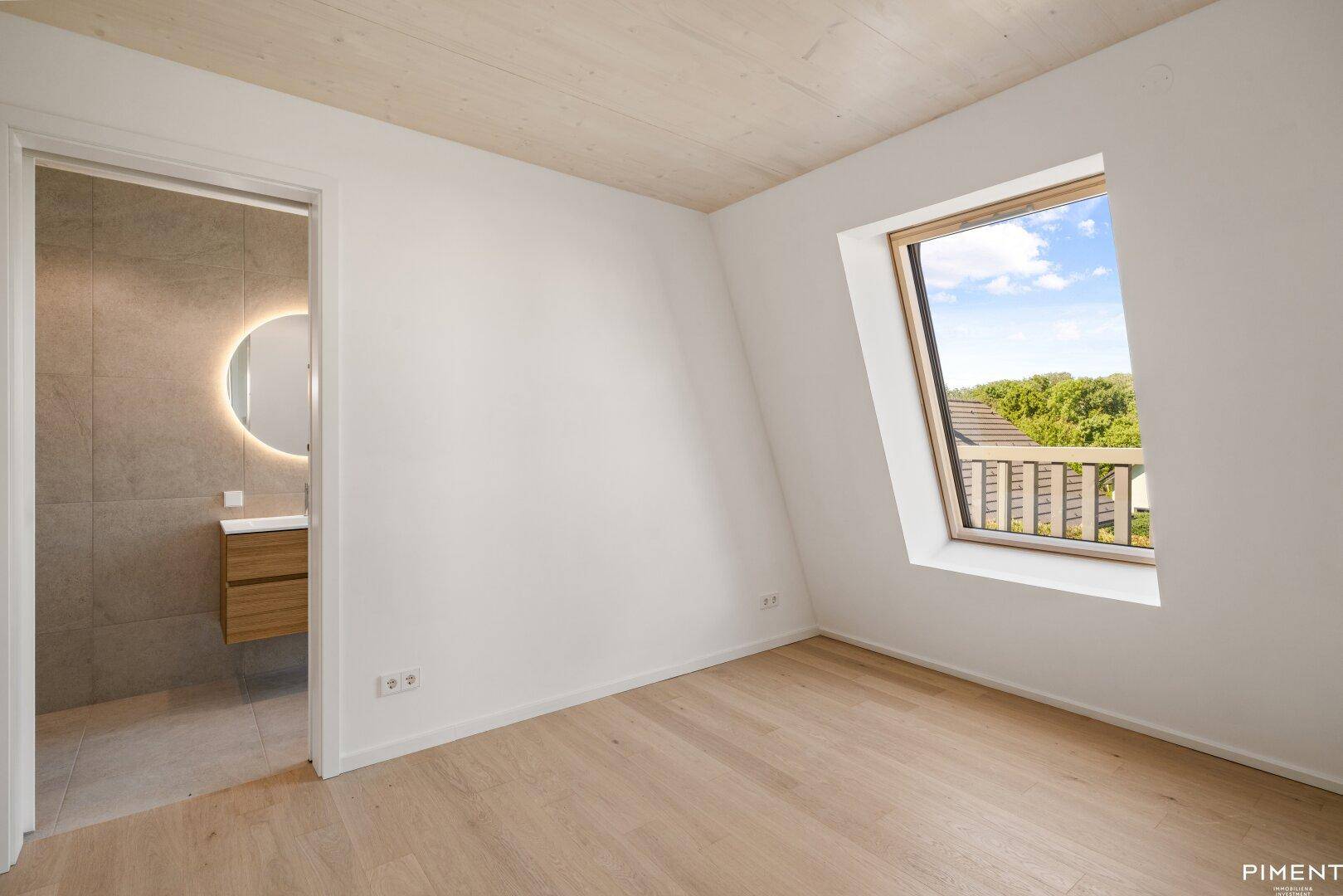 Schlafzimmer mit Holzboden, Dachfenster und direktem Zugang zu einem modernen Badezimmer.