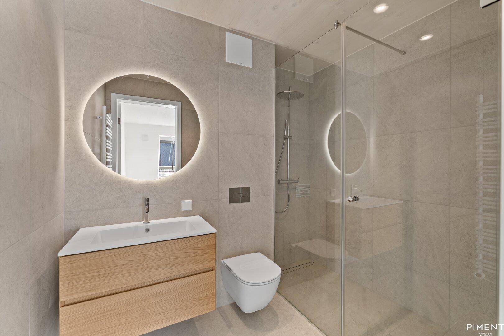 Modernes Badezimmer mit begehbarer Dusche, schwebendem Waschtisch und beleuchtetem Spiegel.