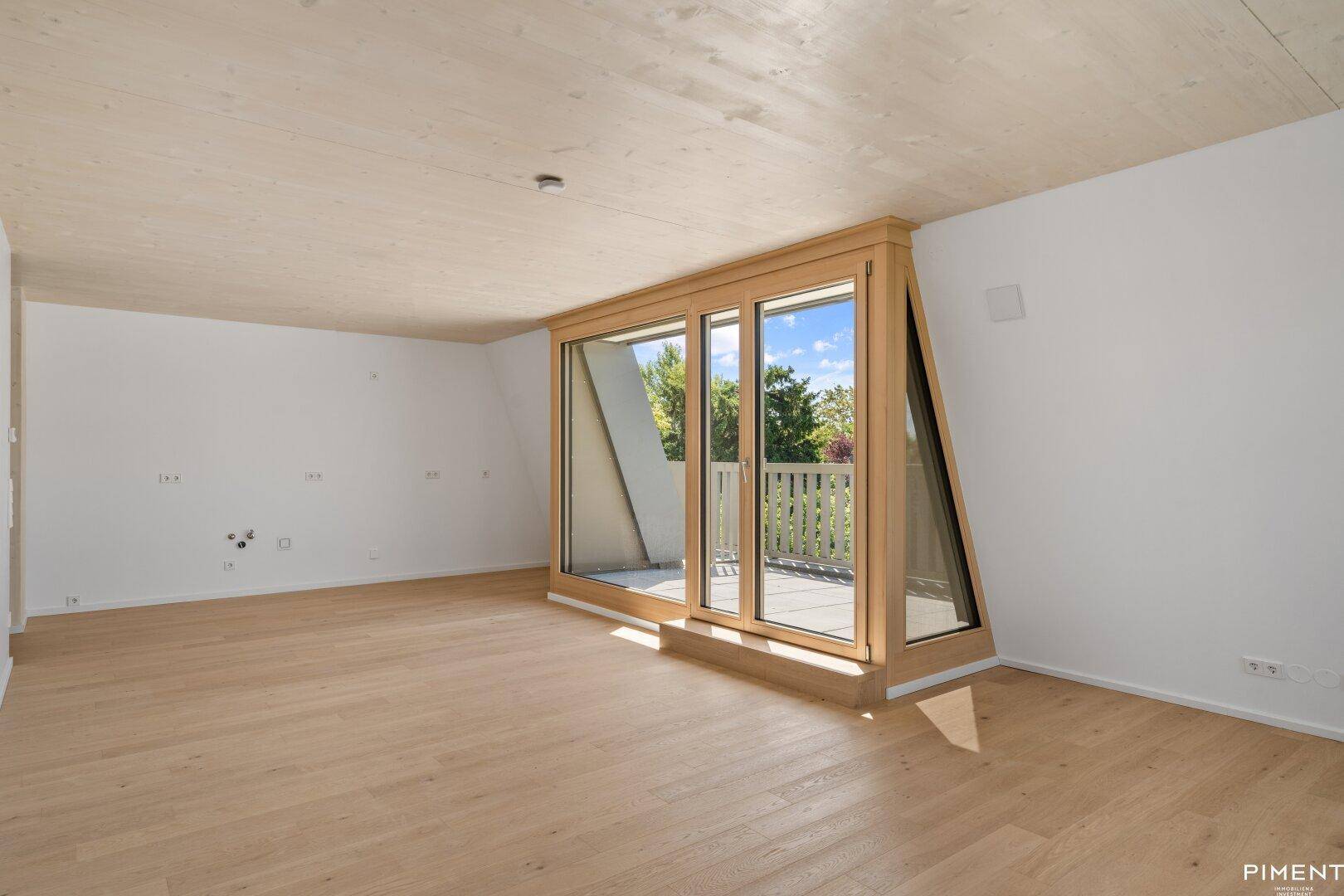Lichtdurchfluteter Raum mit Holzboden, Holzdecke und breiter Fensterfront zum Außenbereich.