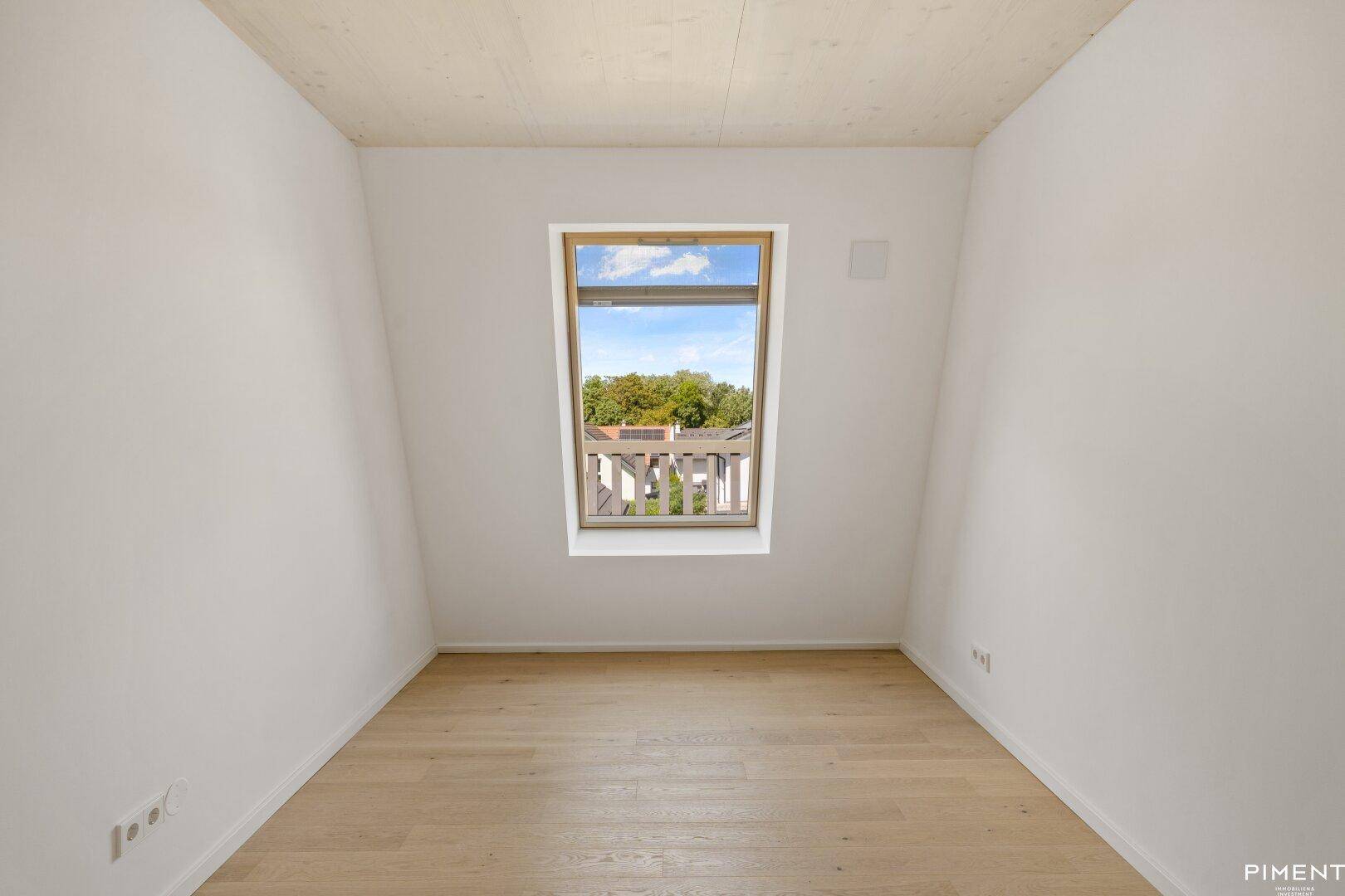 Helles Zimmer mit Holzboden, Holzdecke und einem Dachfenster mit Blick ins Grüne.