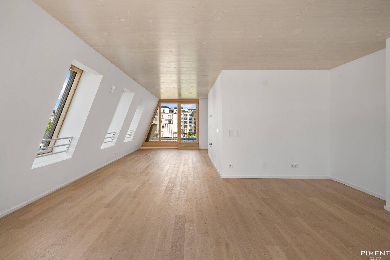 Helles, leeres Zimmer mit Holzboden, Dachschrägen und Zugang zu einem Balkon.
