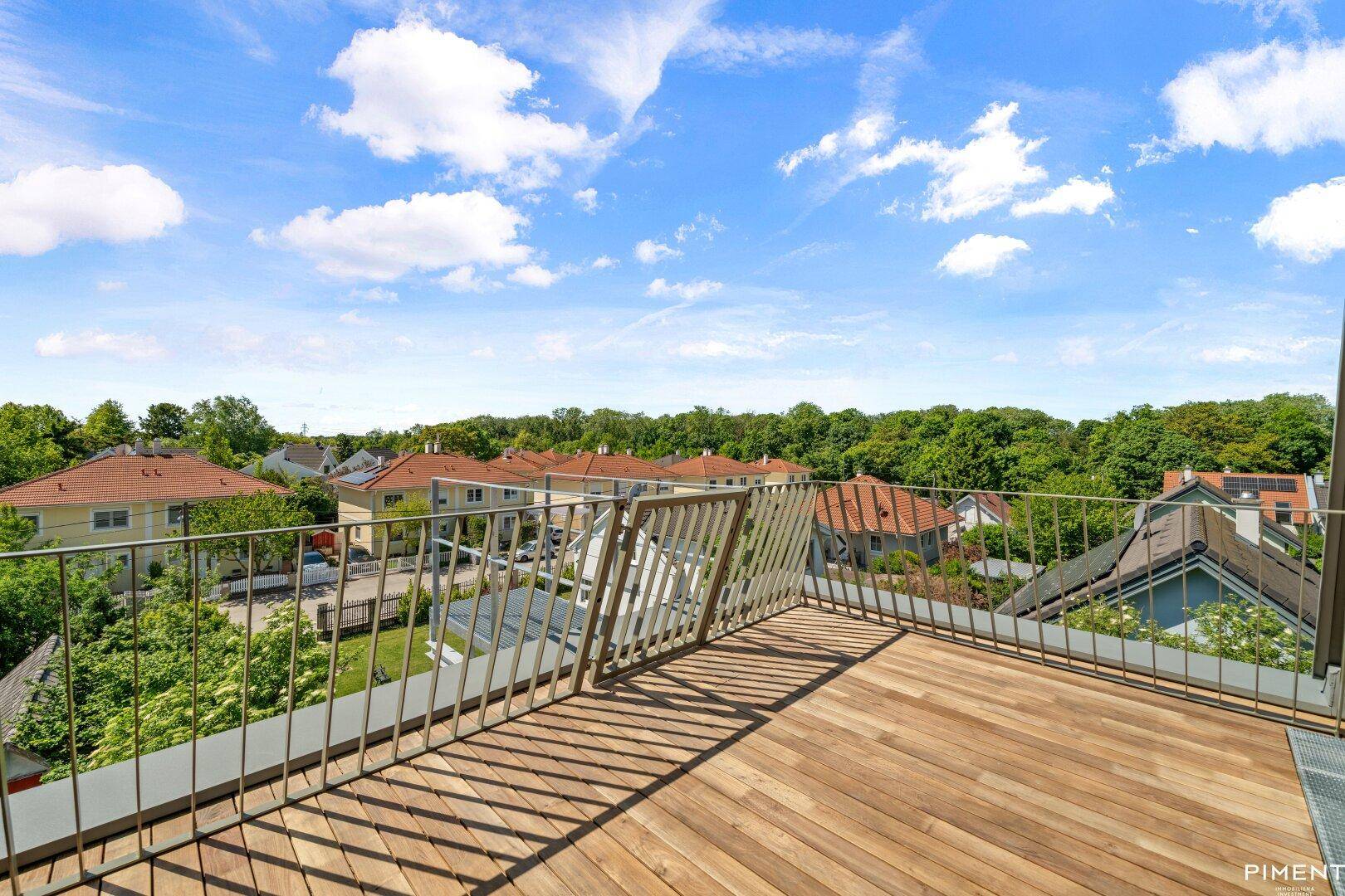 Großer Holzbalkon mit Metallgeländer und weitem Blick über die Dächer und Bäume.