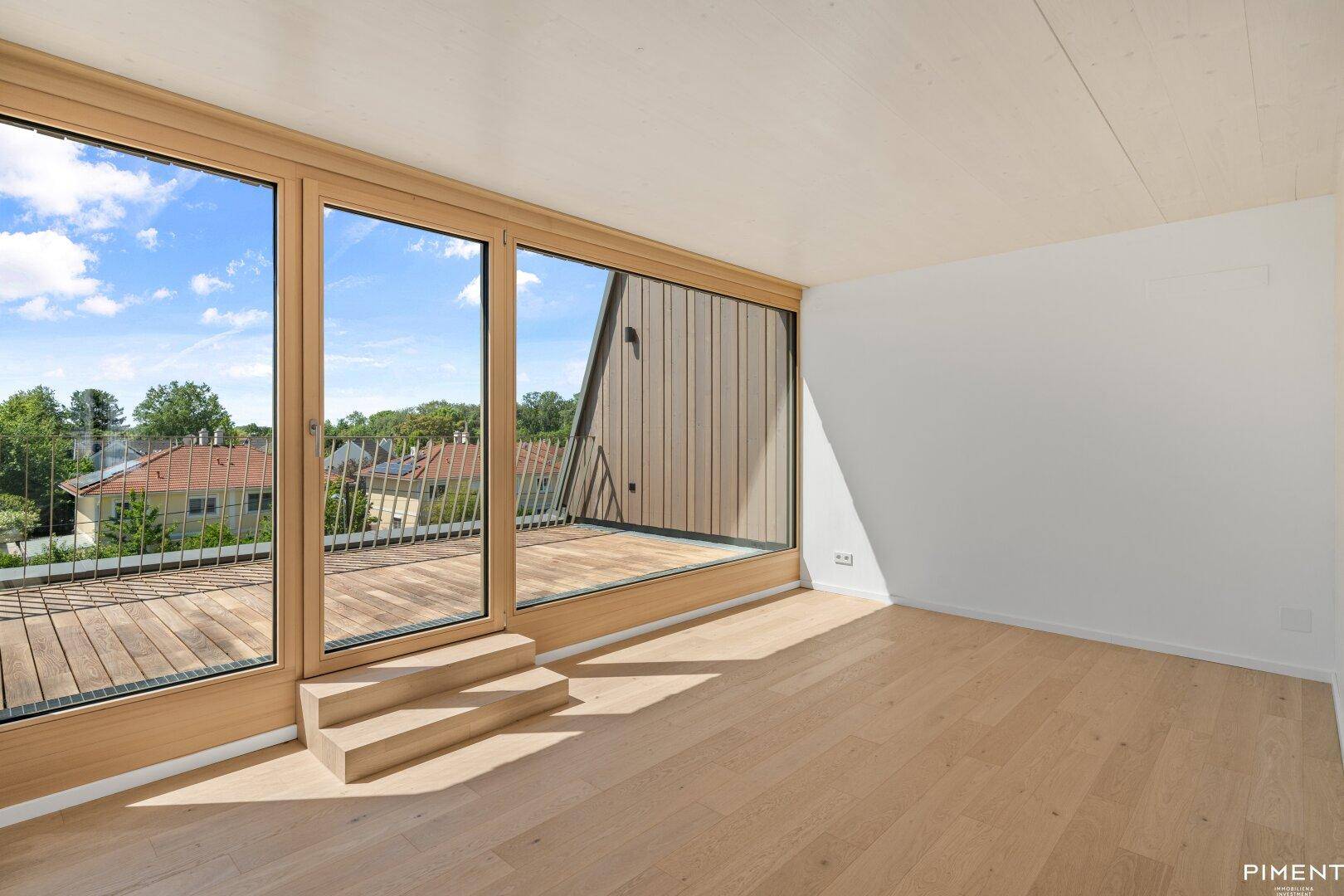 Lichtdurchfluteter Raum mit Holzboden und breiter Fensterfront zur Außenterrasse.