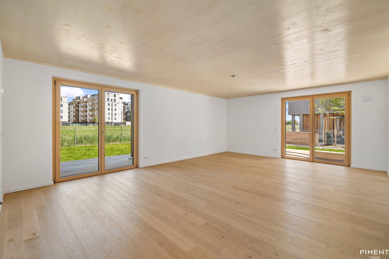 Helles, unmöbliertes Wohnzimmer mit Holzboden und großen Schiebetüren zum Garten.
