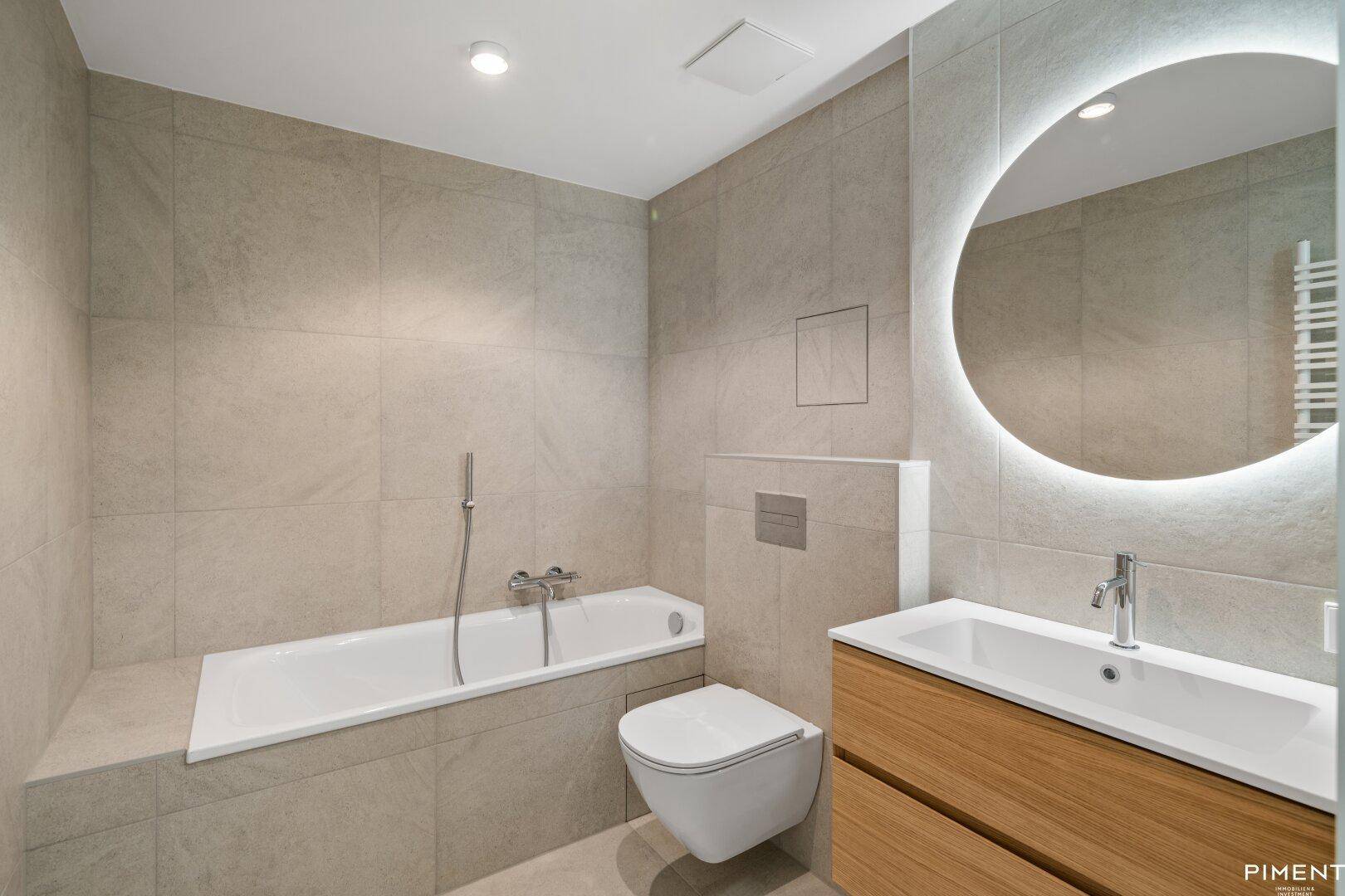 Modernes Badezimmer mit Badewanne, Einzelwaschbecken, Wand-WC und Handtuchheizkörper.