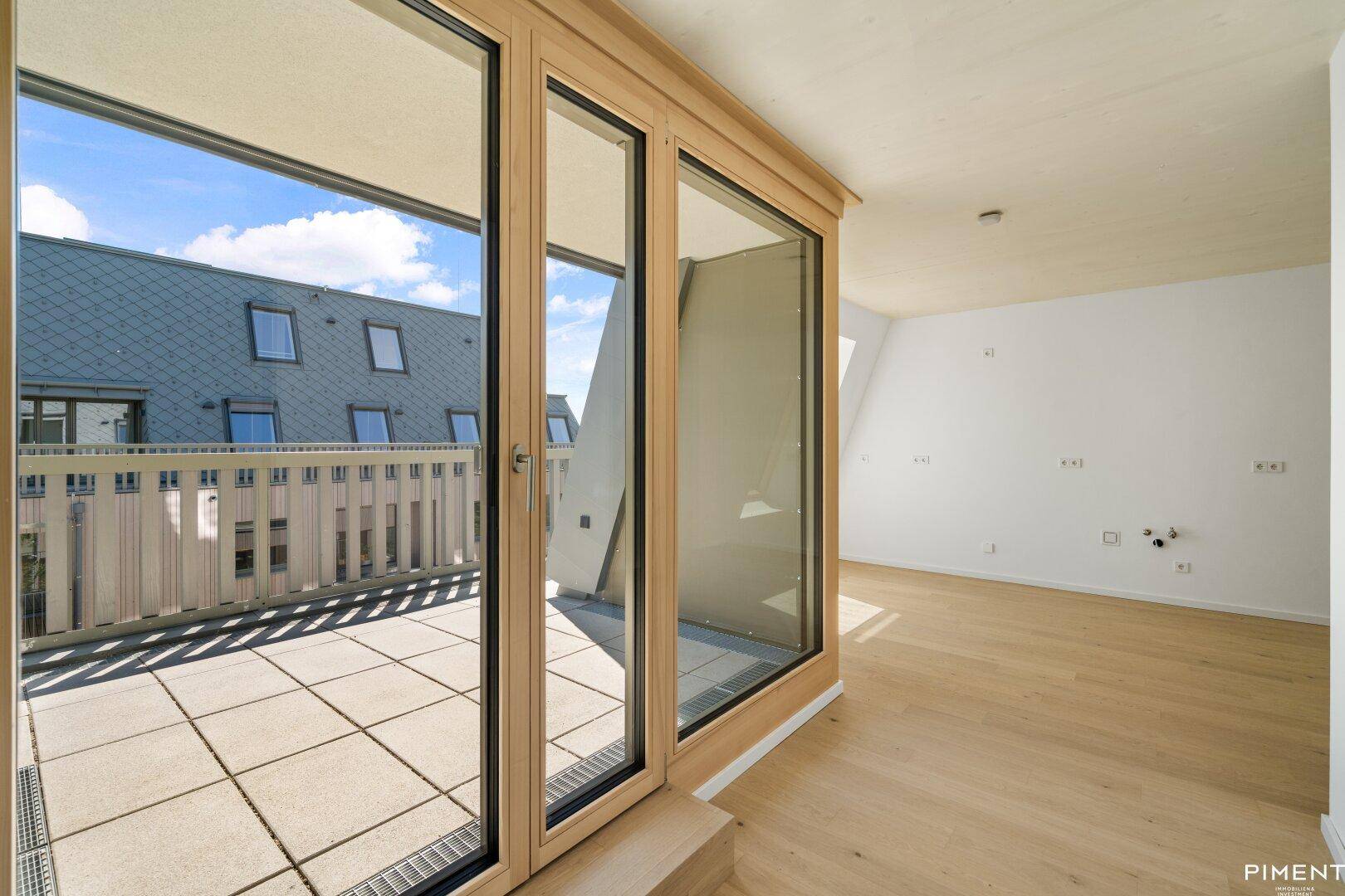Heller Innenraum mit Holzboden und großen Glasfronten, die zu einer geräumigen Terrasse führen.