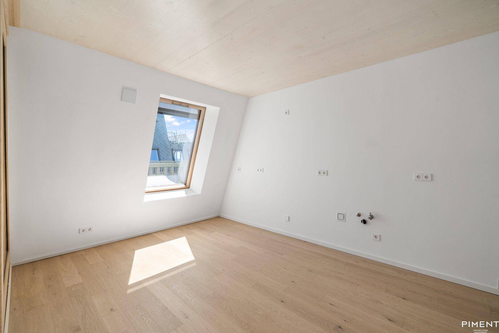 Helles, unmöbliertes Zimmer mit Holzboden und schrägen Wänden, ideal für ein Schlafzimmer.