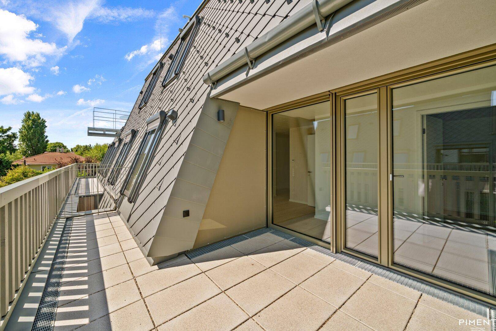 Geräumige Dachterrasse mit Fliesenboden und Blick auf die Umgebung und das moderne Gebäude.