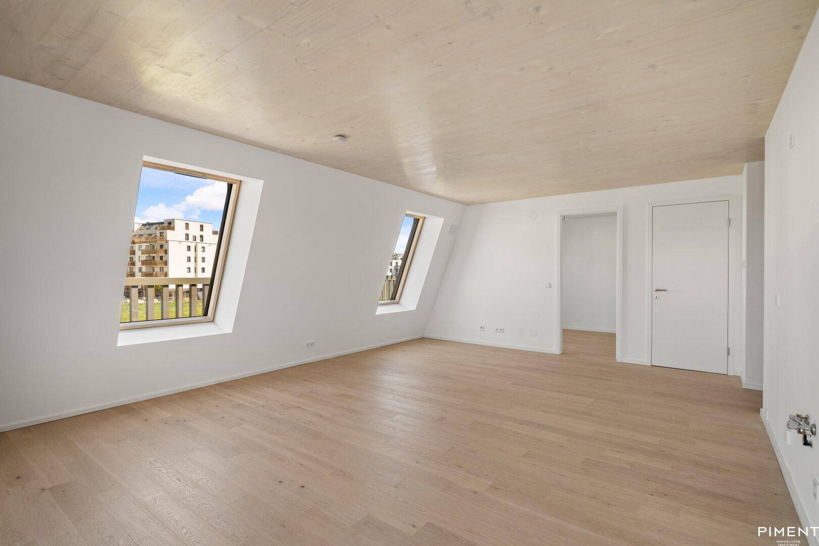 Geräumiges, unmöbliertes Zimmer mit Holzboden, Dachfenstern und weiß gestrichenen Wänden.