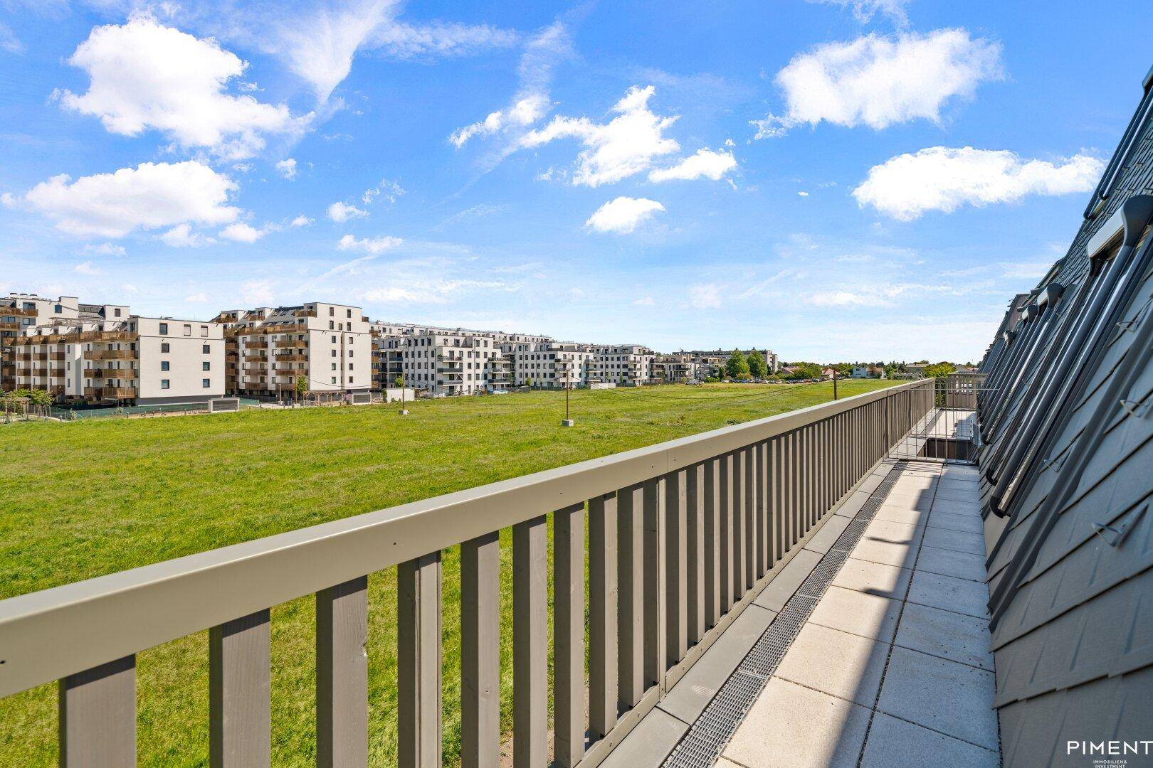Weitläufiger Blick von der Dachterrasse über grüne Felder und moderne Wohngebäude.