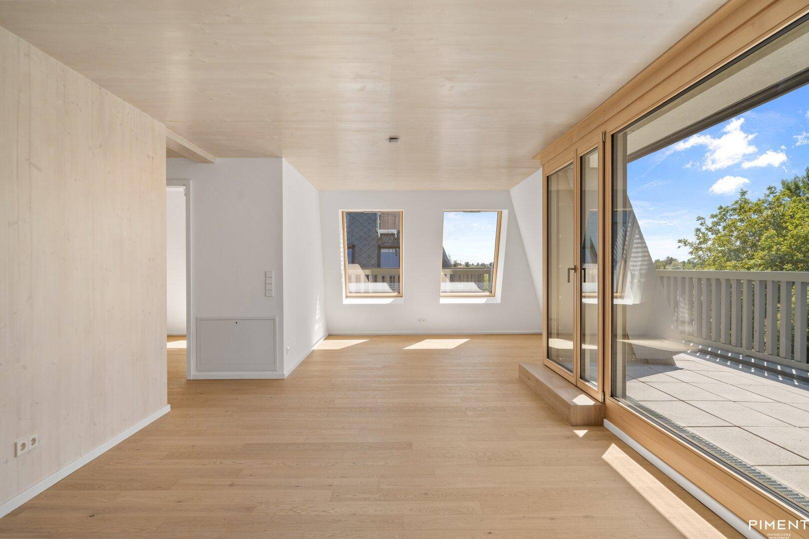 Lichtdurchfluteter Raum mit Holzboden, Dachfenstern und Zugang zur Außenterrasse.
