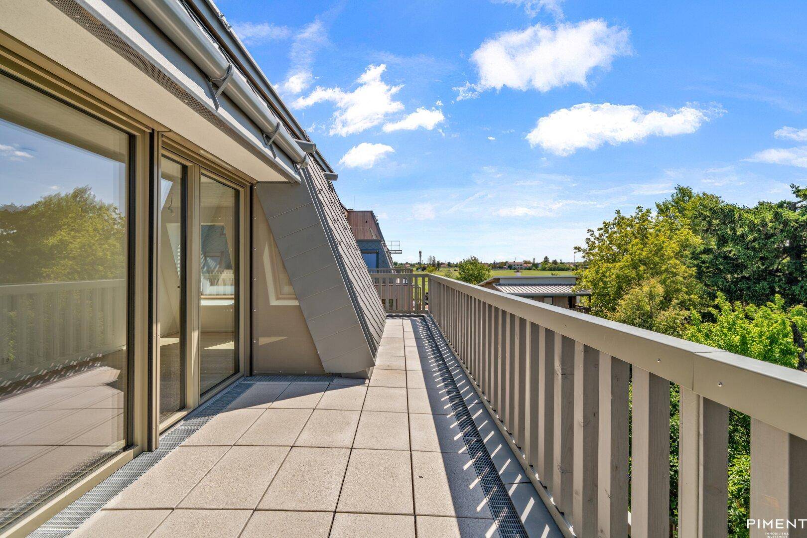 Lange Dachterrasse mit Fliesenboden und Geländer, bietet einen weiten Blick ins Grüne.