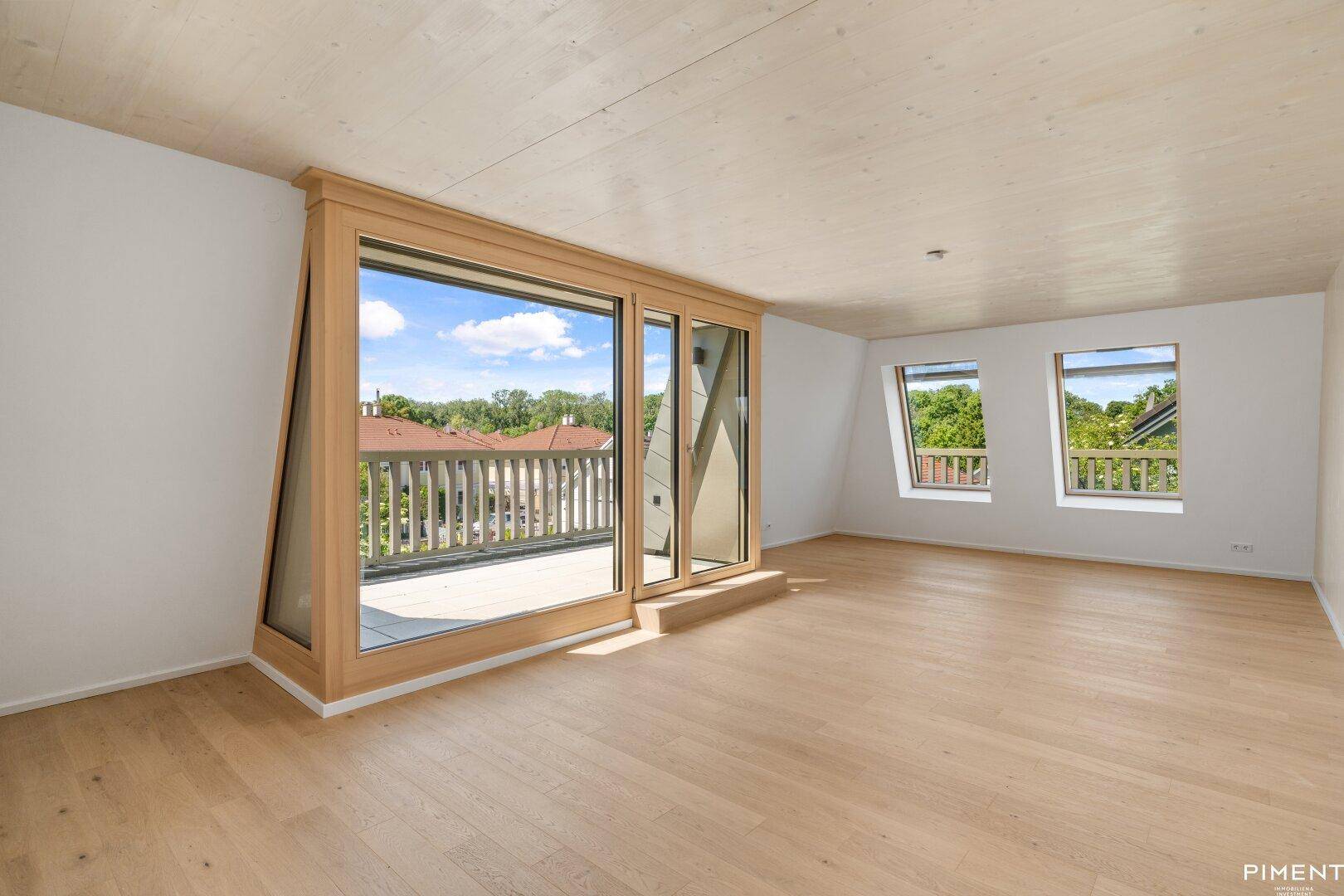 Helles Zimmer im Dachgeschoss mit Holzboden, großen Fenstern und Zugang zu einem Balkon.