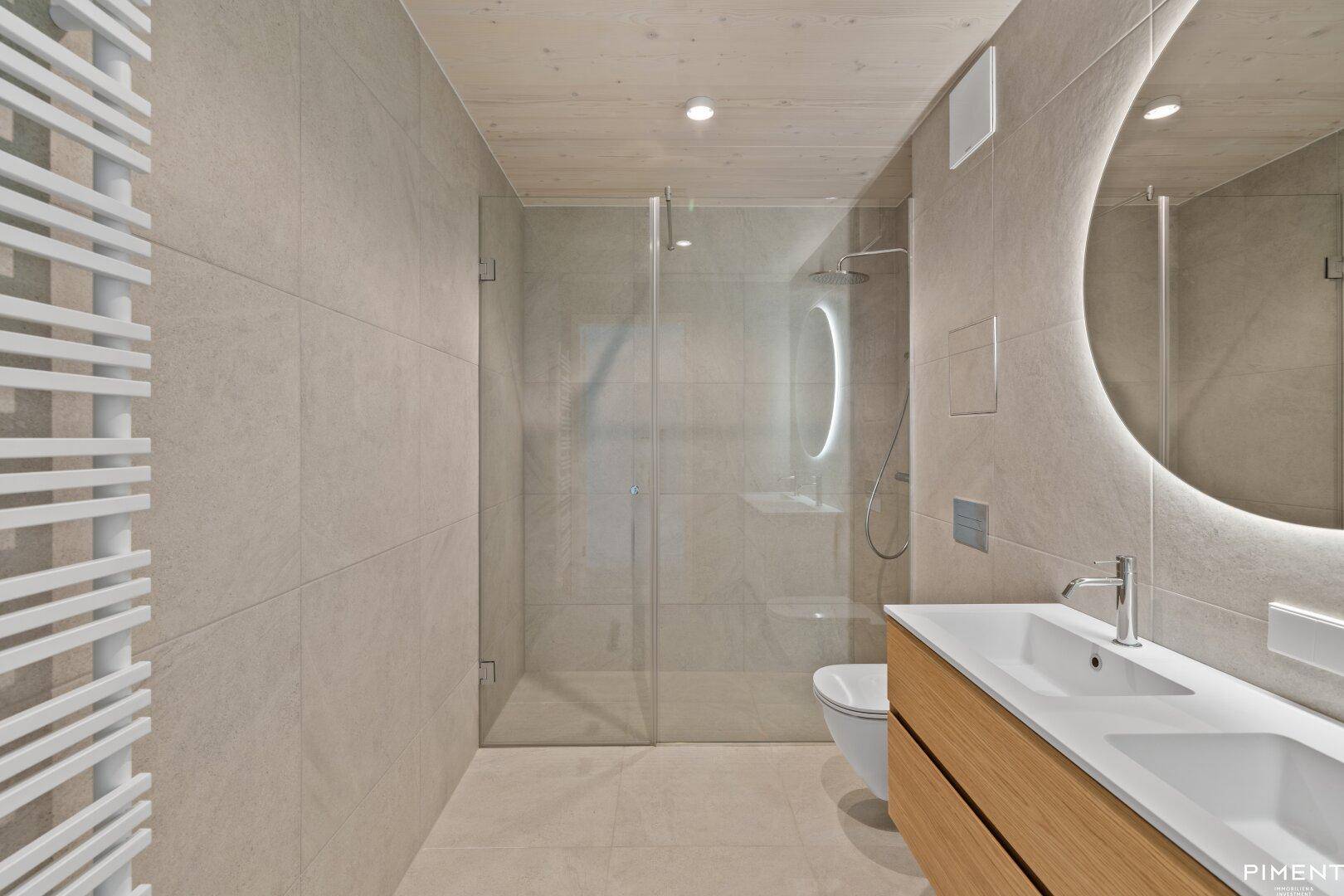 Modernes Badezimmer mit begehbarer Dusche, Doppelwaschbecken und beleuchtetem Spiegel.