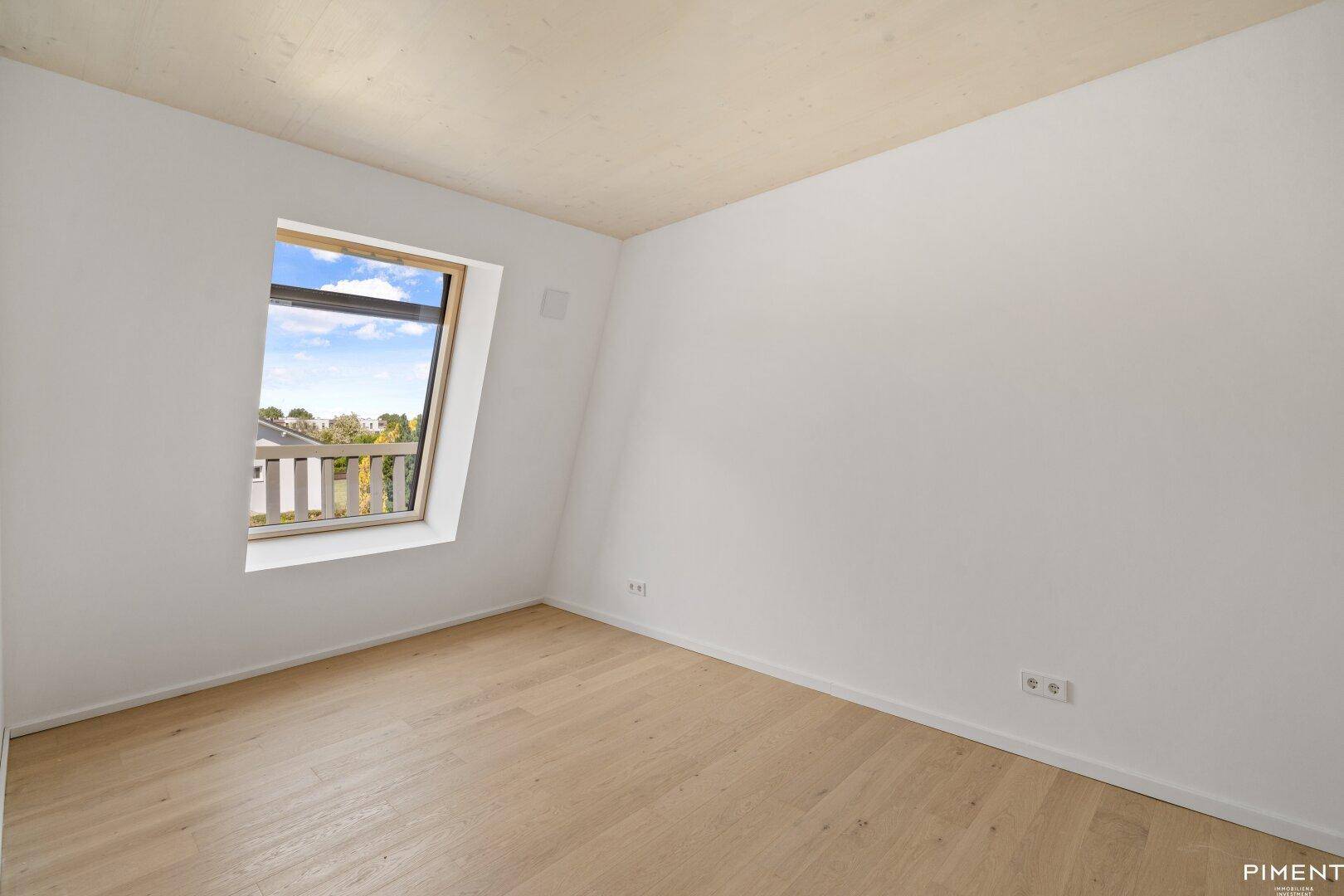 Helles Schlafzimmer mit Holzboden, Dachschräge und einem Fenster mit Blick ins Grüne.