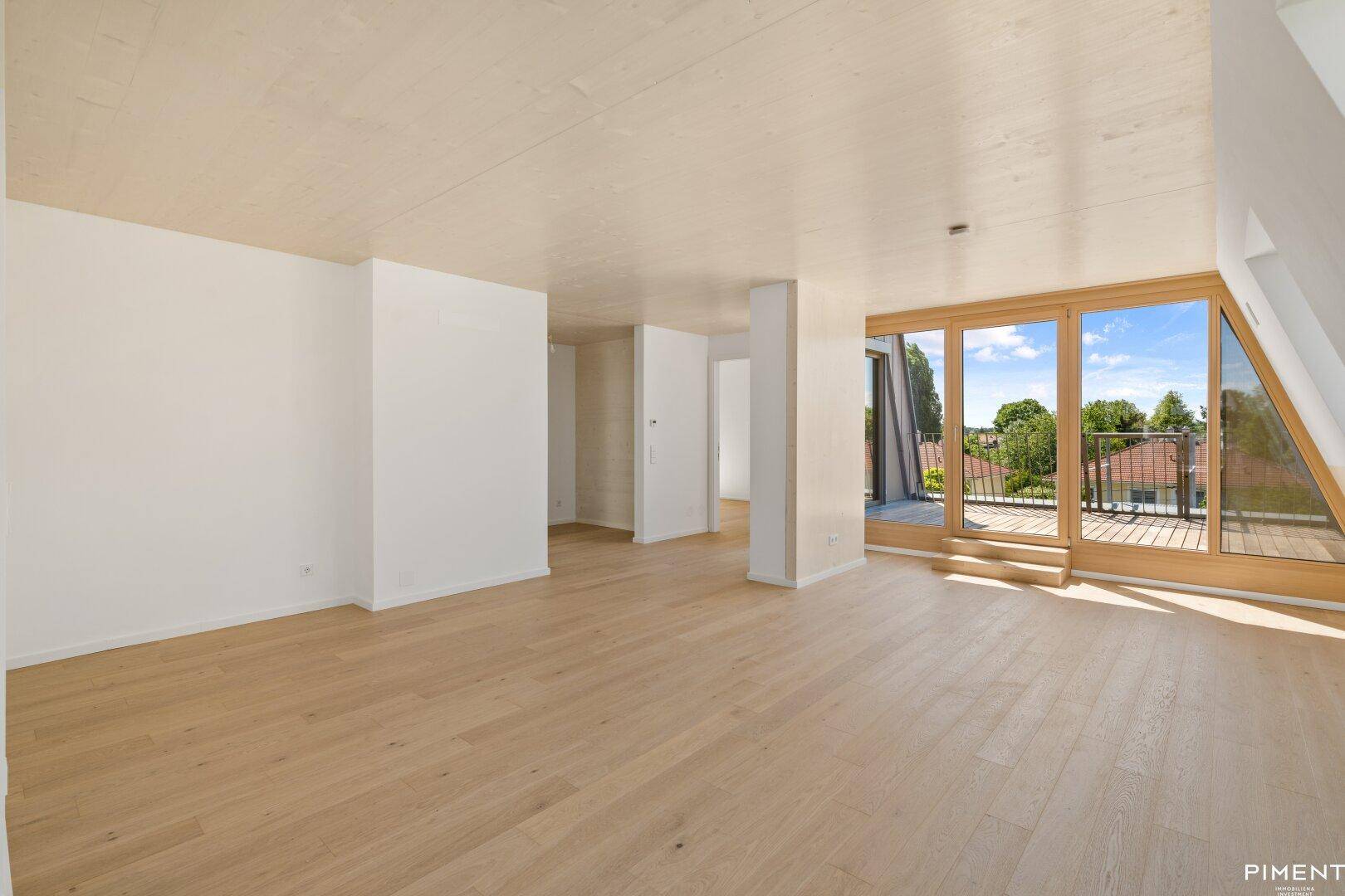 Helles, leeres Zimmer mit Holzboden und Zugang zu einem Balkon mit Weitblick.