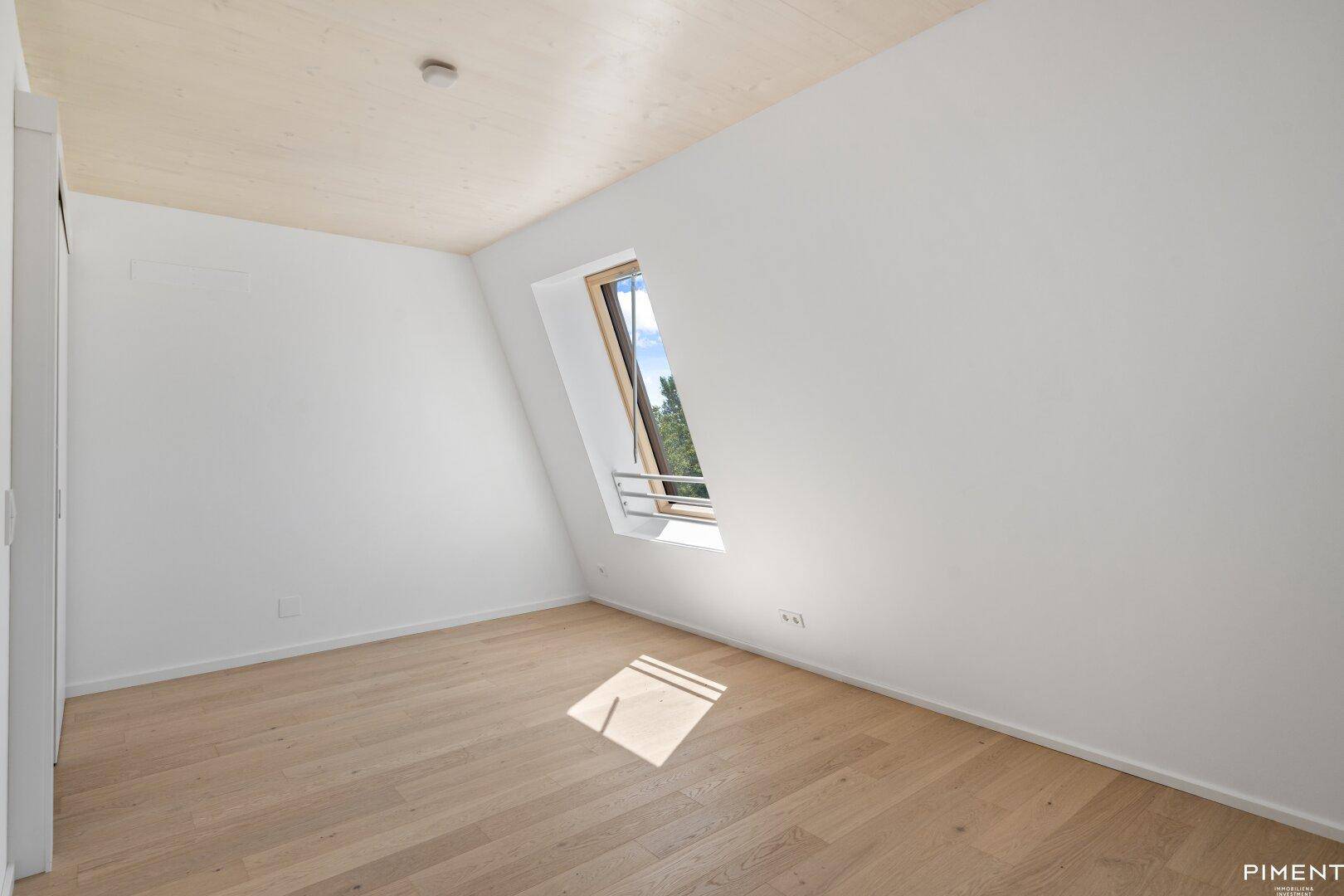 Ruhiges Schlafzimmer mit Holzboden und Dachschrägenfenster, ideal für erholsame Nächte.