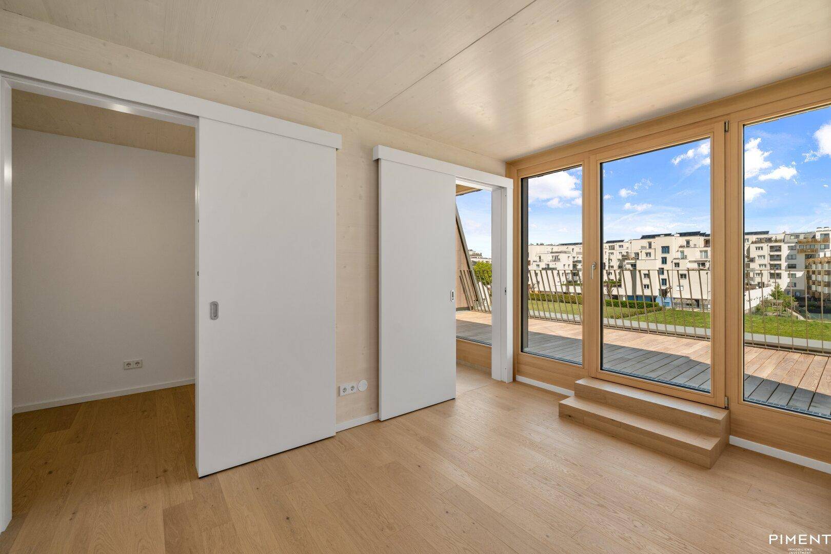 Geräumiges Zimmer mit Schiebetüren, Holzboden und Zugang zu einem Balkon mit Stadtblick.
