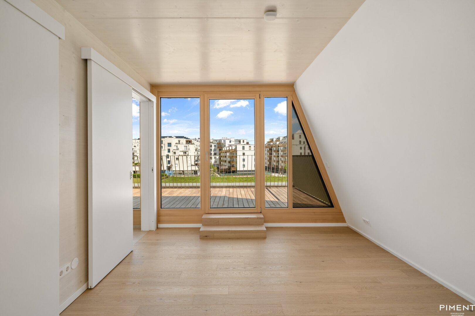 Helles Schlafzimmer mit Holzboden, großen Fenstern und Blick auf die umliegende Bebauung.