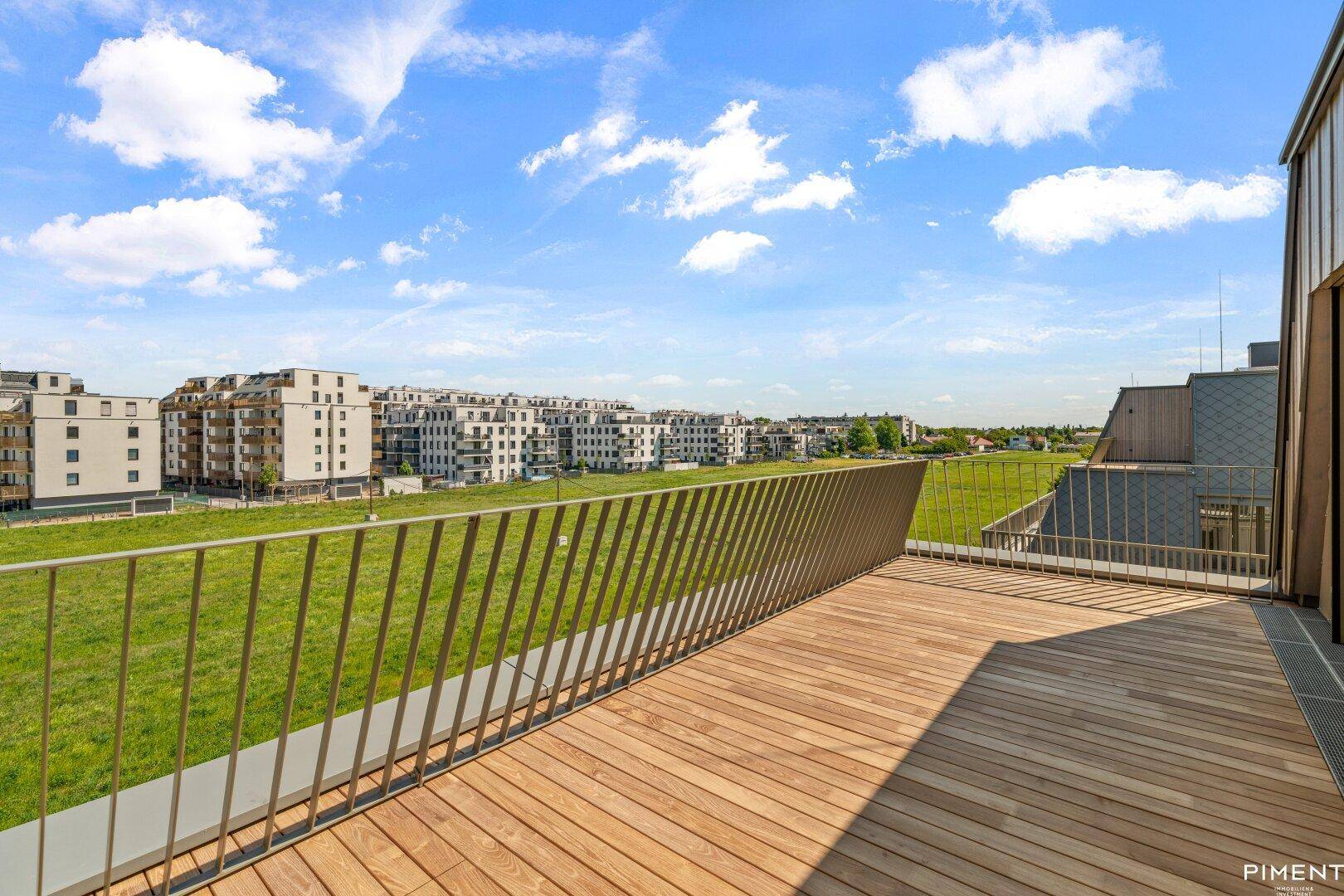 Weitläufige Holzterrasse mit Blick auf grüne Wiesen und moderne Wohngebäude.