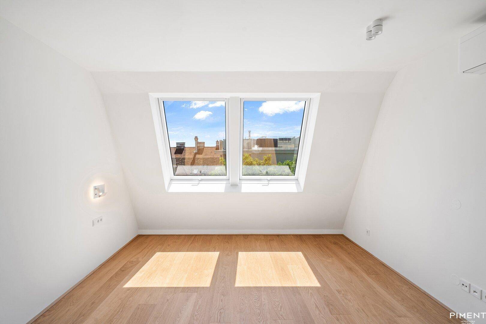 Helles Schlafzimmer mit Holzboden und zwei großen Dachfenstern.
