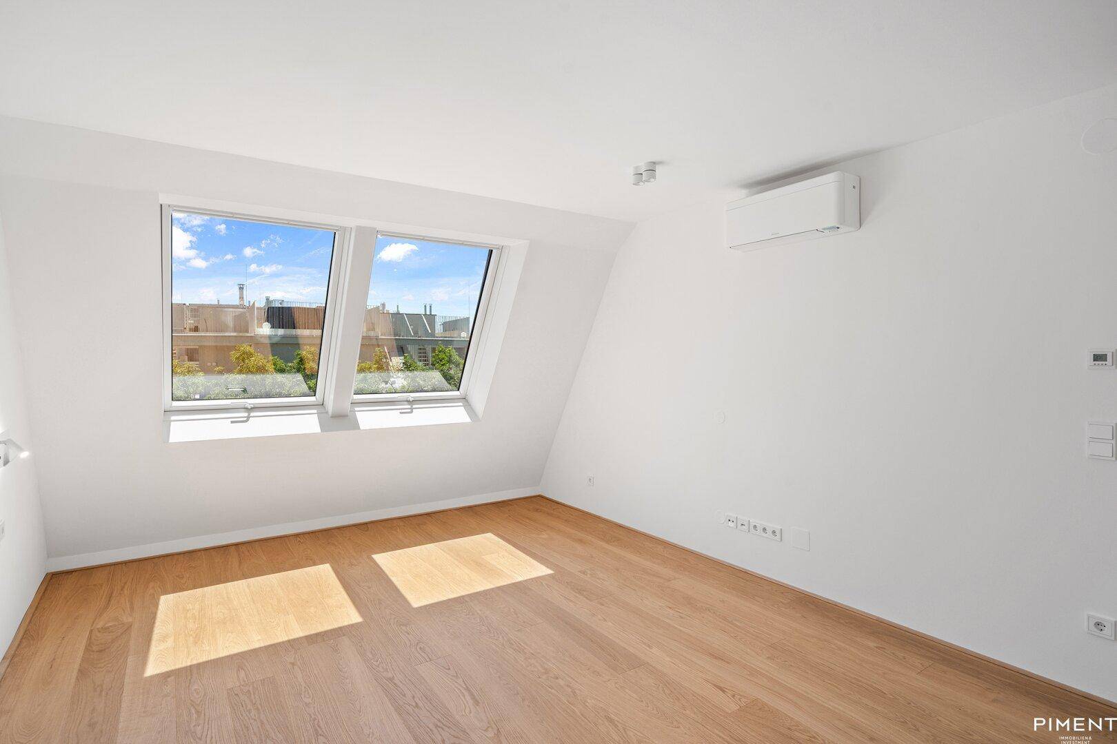 Geräumiges Schlafzimmer mit Holzboden, Dachschräge und zwei Dachfenstern.