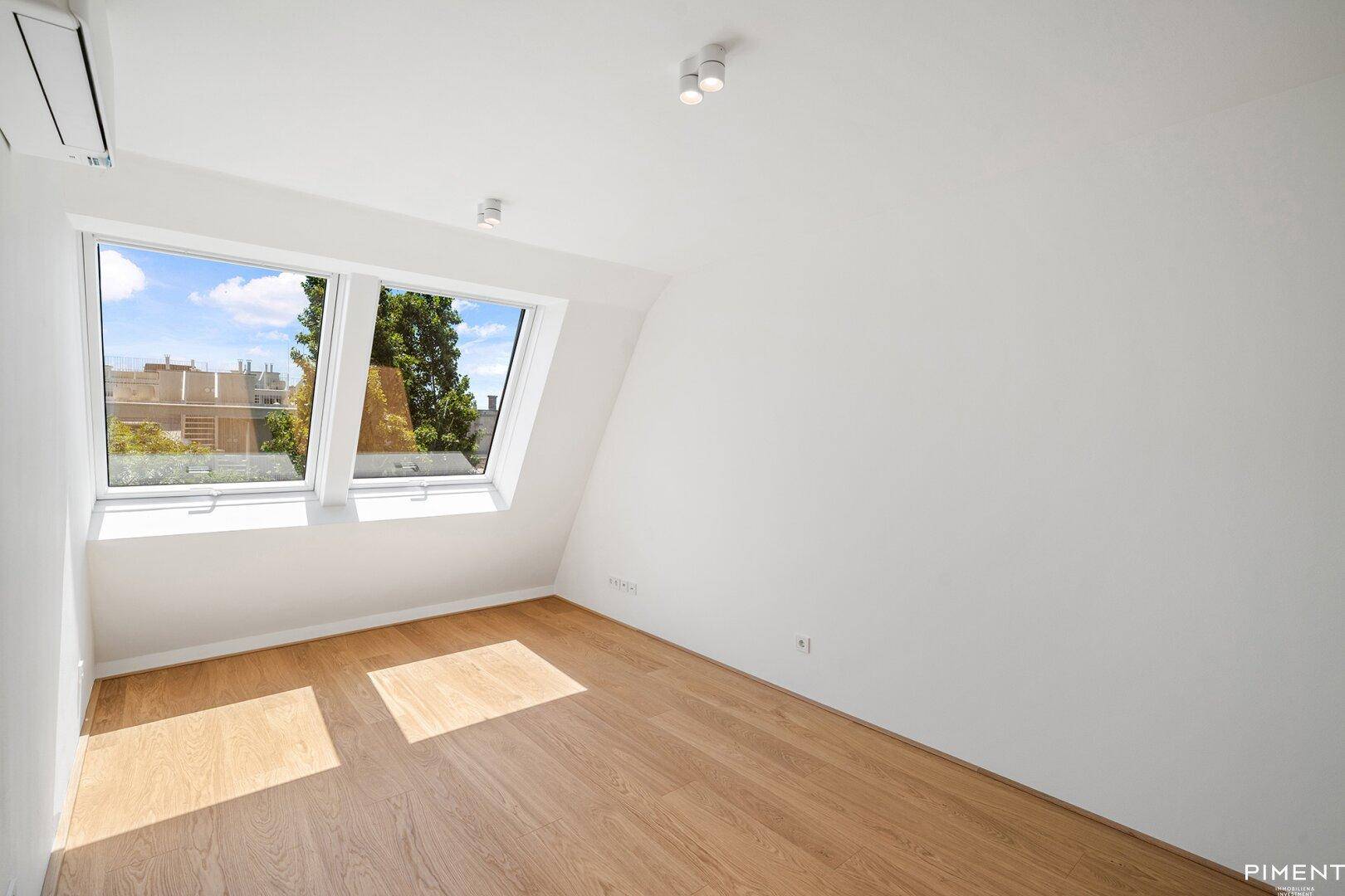 Lichtdurchflutetes Schlafzimmer mit Holzboden, Dachschräge und Blick ins Grüne.