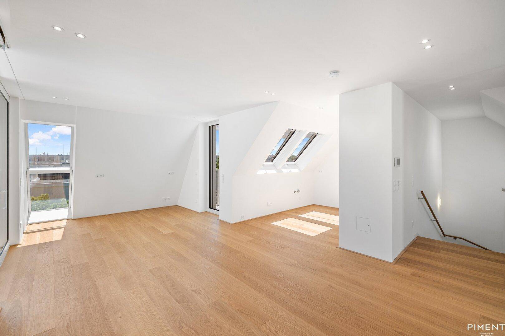 Heller Wohnbereich mit Holzboden, Dachfenstern und Treppenzugang.